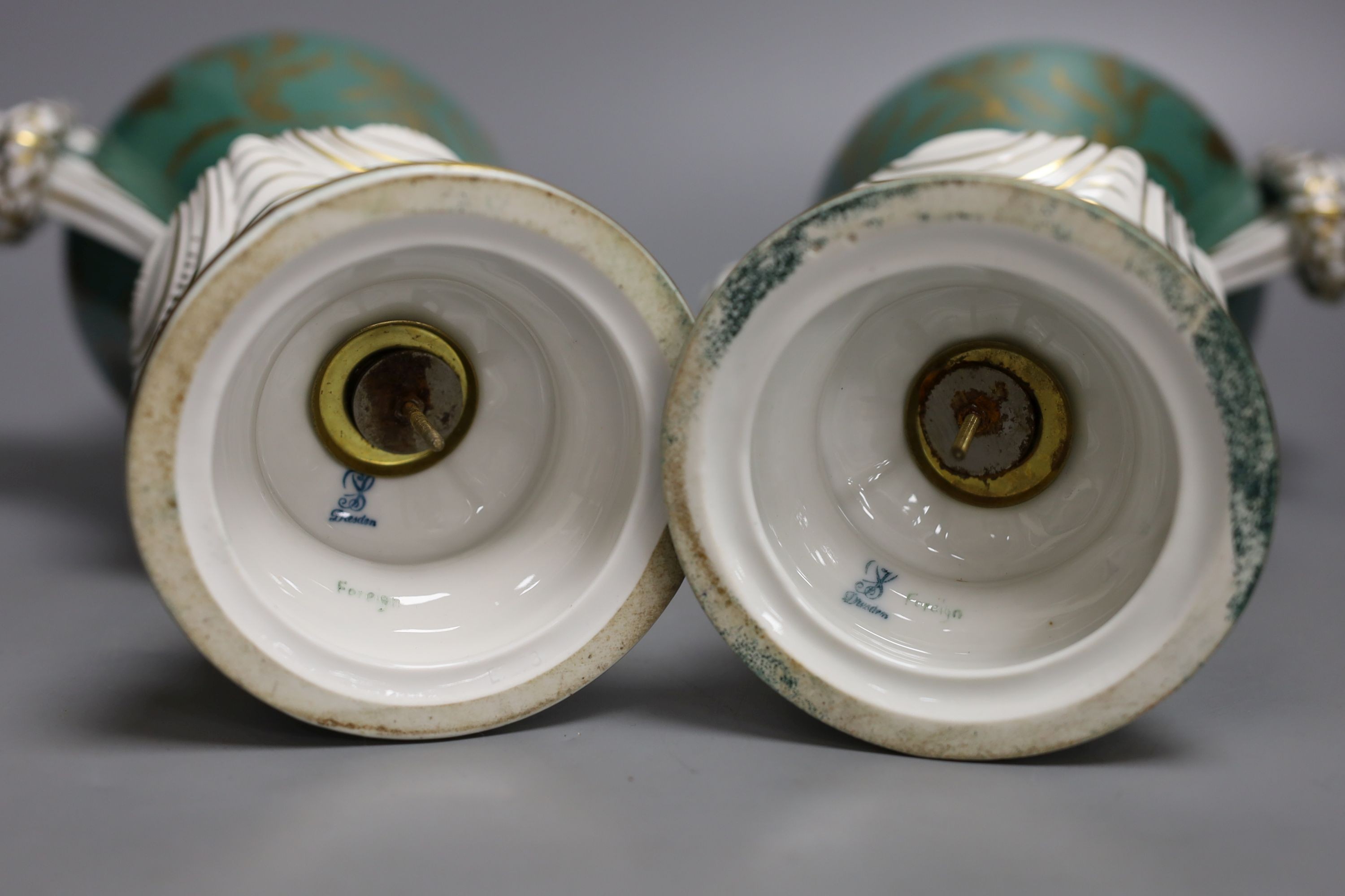 A pair of early 20th century Dresden vases painted with landscapes on an avocado green ground, 24cm high together with a German bottle vase and cover painted with four landscape panels separated by blue and white panels